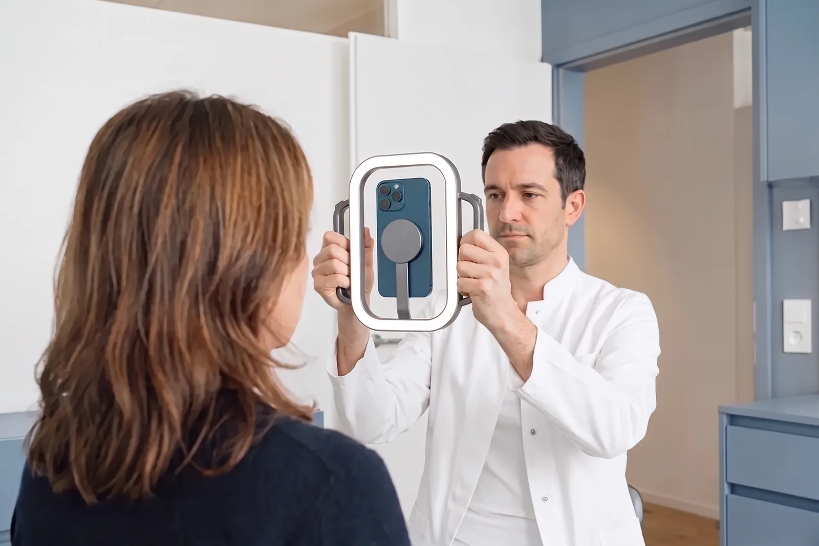 A clinician holds the evooia Light with both hands, an iPhone mounted in its frame, while photographing a patient's face in a treatment room